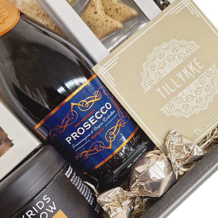 Send en gavekurv og ønske tillykke. Fin og festlig kurv med skønne prosecco bobler, dansk chokolade fra Summerbird, sprøde kiksekugler og Lakrids by Bülow