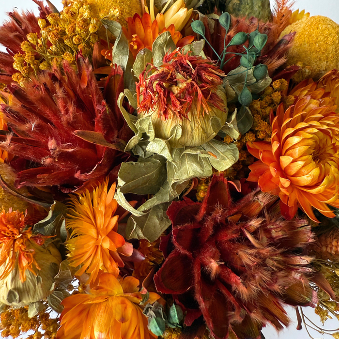 Frodig mini-buket i varme orange farver, håndbundet af tørrede og præserverede blomster, der holder sig smuk i lang tid.