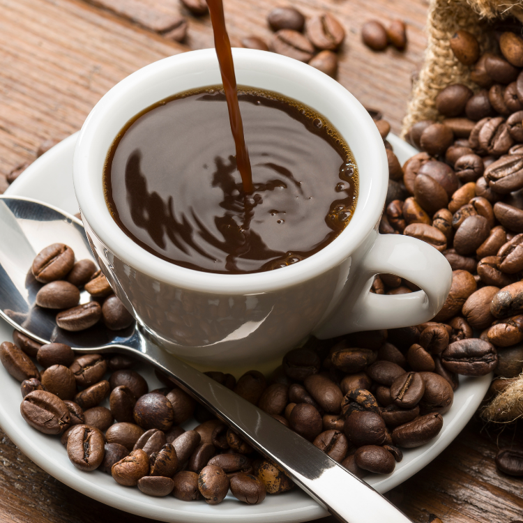 Nyskænket sort kaffe i hvid kop omgivet af hele kaffebønner på et rustikt træbord.