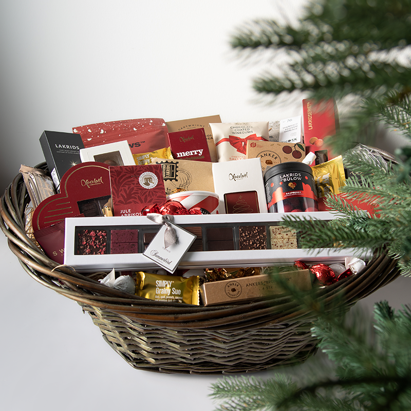 Stor luksuskurv fyldt med chokolade, lakrids og håndplukkede delikatesser, smukt præsenteret i en fletkurv indpakket i cellofan og pyntet med gavebånd