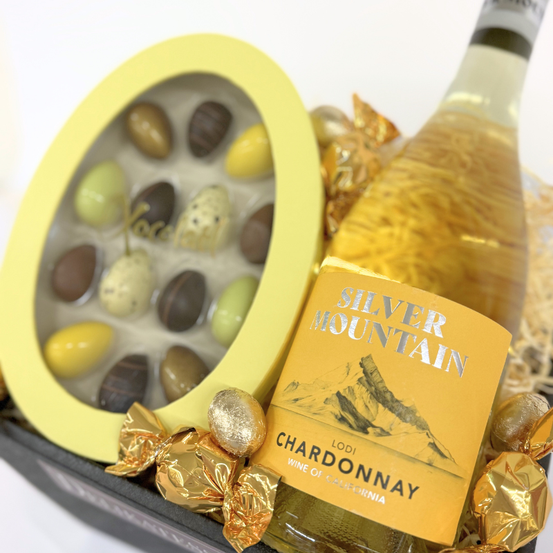 Gavekurv til påske med tropisk Chardonnay, fyldte chokolader, chokoladekugler og dekorativ indpakning klar til påskebordet.