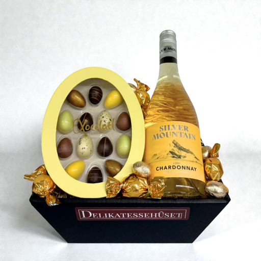 Påskegavekurv med californisk Chardonnay, fyldte påskeæg, chokoladekugler og gaveæske med 14 store påskeæg, pakket i kurv med træuld og cellofan.