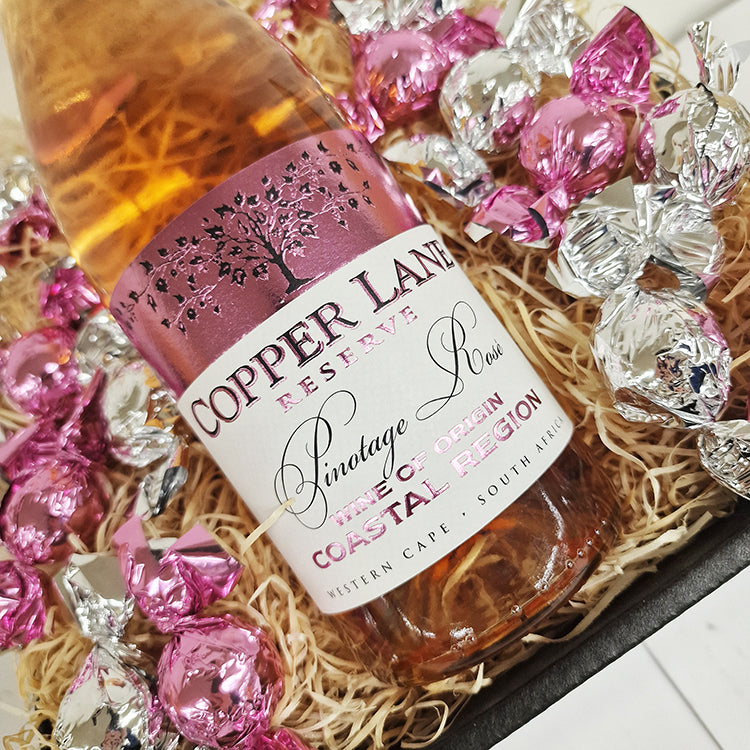 Gavekurv med Copper Lane Pinotage Rosé og indpakkede chokoladekugler i træuld.