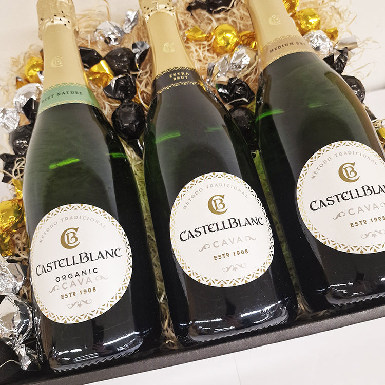 Gavekurv med tre flasker Castellblanc Cava mousserende vin omgivet af lækre chokolader.