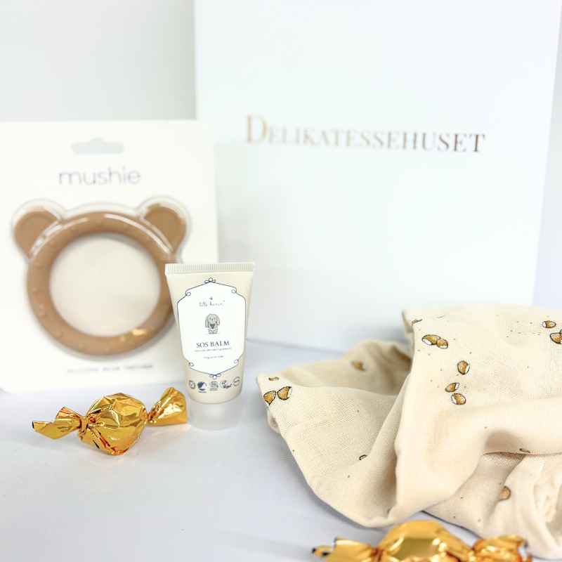 Fin baby gavepose med SAGA COPENHAGEN stofble, plejende SOS Balm, Mushie bidering med sansedetaljer og chokoladekugler – perfekt til barsel eller babyshower.