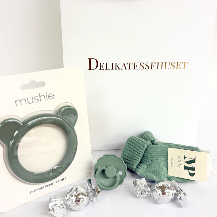 Grøn barselsgave i gavepose med strømper til baby, FRIGG sut, Mushie bidering og 2 chokoladekugler – perfekt som babyshowergave eller gave til nybagte forældre.