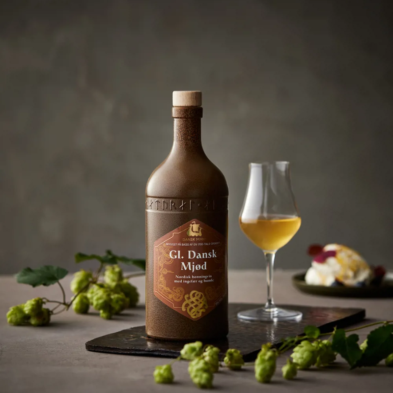 En flaske Gl. Dansk Mjød fra Dansk Mjød ved siden af et glas med honningvin.