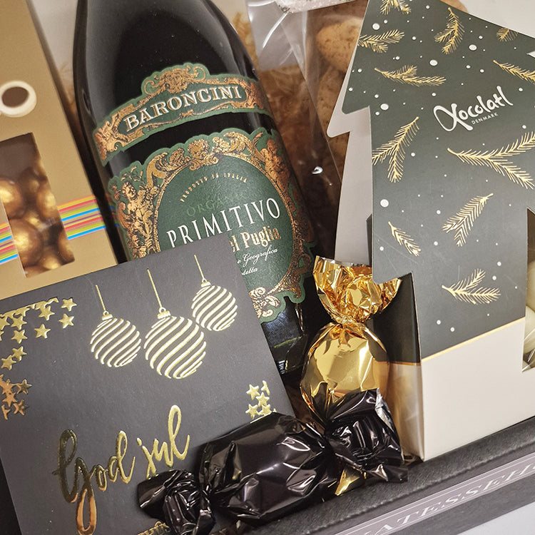 Tæt på af en flot julekurv med Primitivo rødvin, chokolade og et personligt julekort.