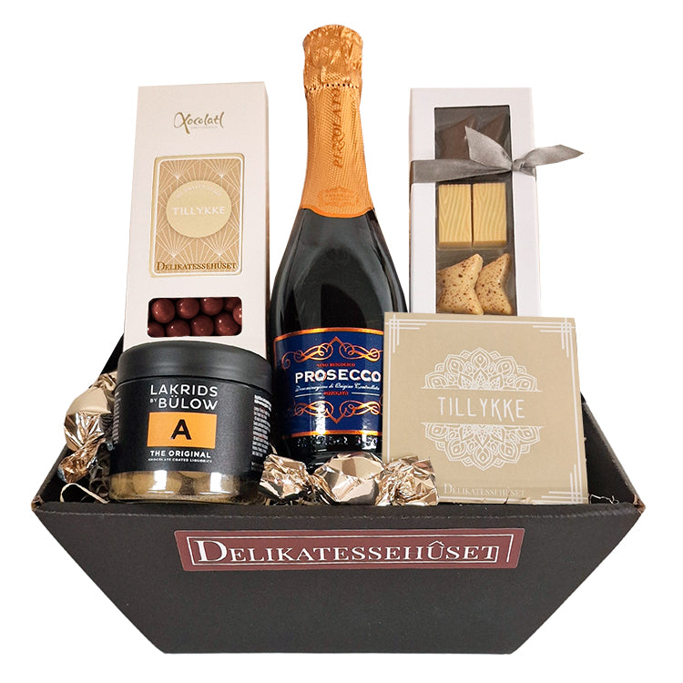 Send en gavekurv og ønske tillykke. Fin og festlig kurv med skønne prosecco bobler, dansk chokolade fra Summerbird, sprøde kiksekugler og Lakrids by Bülow