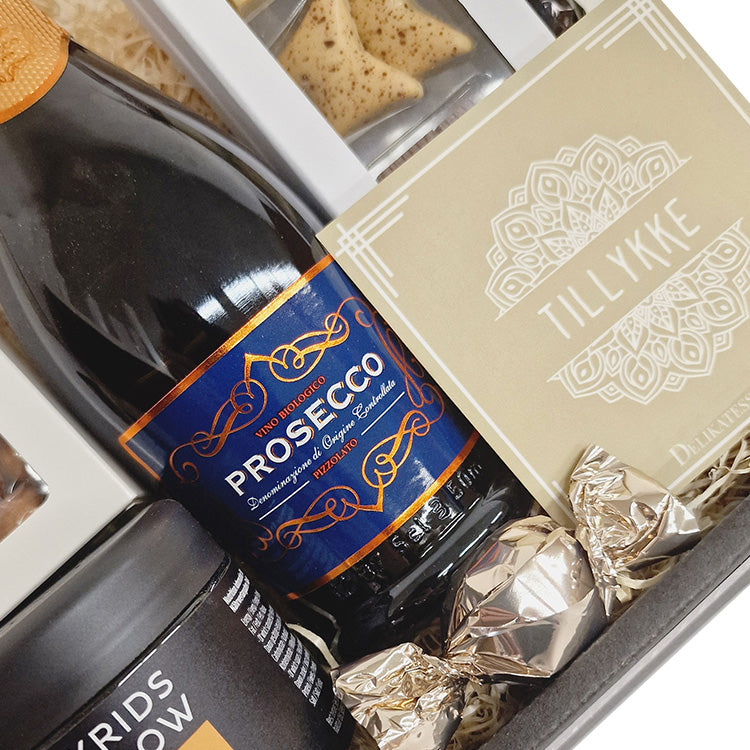 Send en gavekurv og ønske tillykke. Fin og festlig kurv med skønne prosecco bobler, dansk chokolade fra Summerbird, sprøde kiksekugler og Lakrids by Bülow