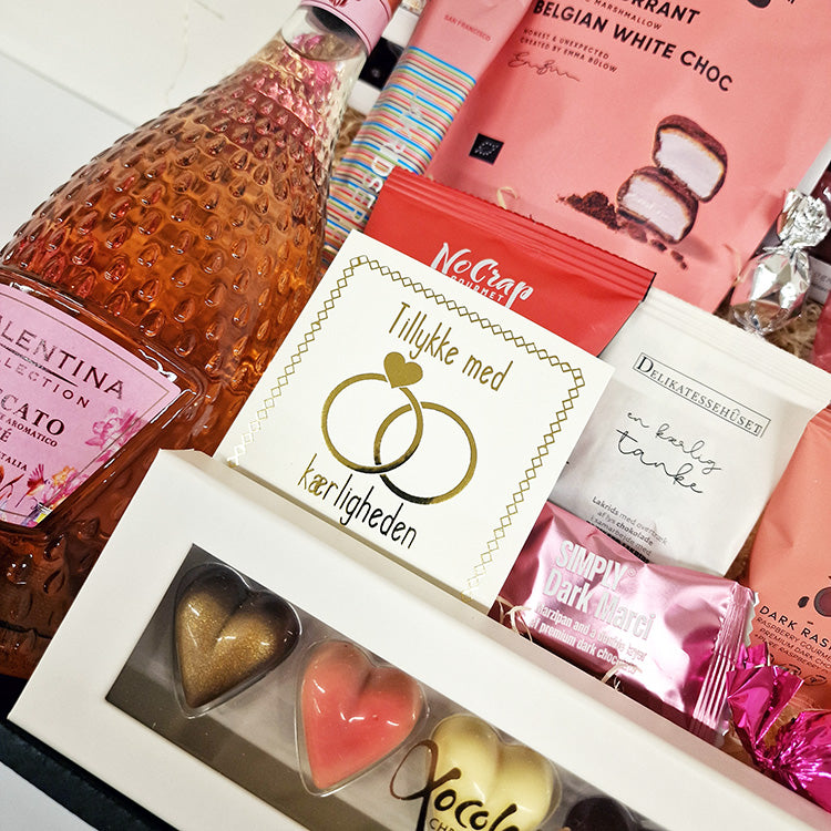 Lyserød gavekurv med Moscato, chokoladehjerter og et kort med teksten Tillykke med kærligheden.