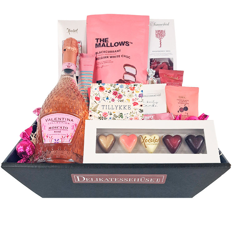 Lyserød gavekurv med Moscato, chokoladehjerter og søde sager med teksten Tillykke.