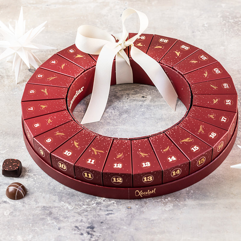 Julekalender fra Xocolatl – 24 æsker samlet i en smuk krans, hver med to fyldte danske chokolader med bl.a. karamel, ganache og nougat.	