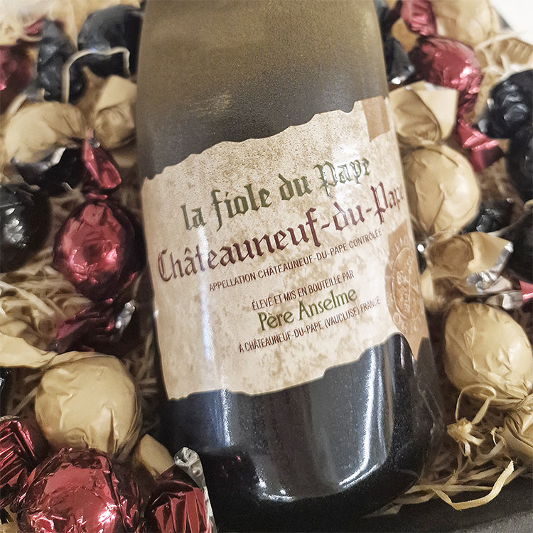 Nærbillede af Chateauneuf du Pape vinflaske i gavekurv omgivet af indpakket chokolade.