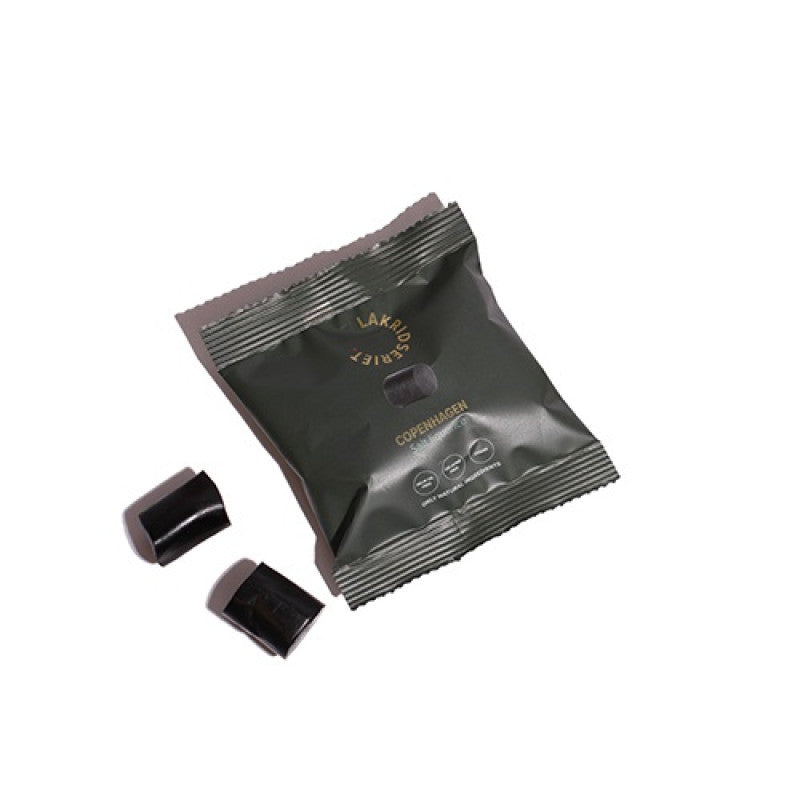 Grøn pose med saltlakrids fra Lakridseriet og to sorte lakridsstykker på hvid baggrund.