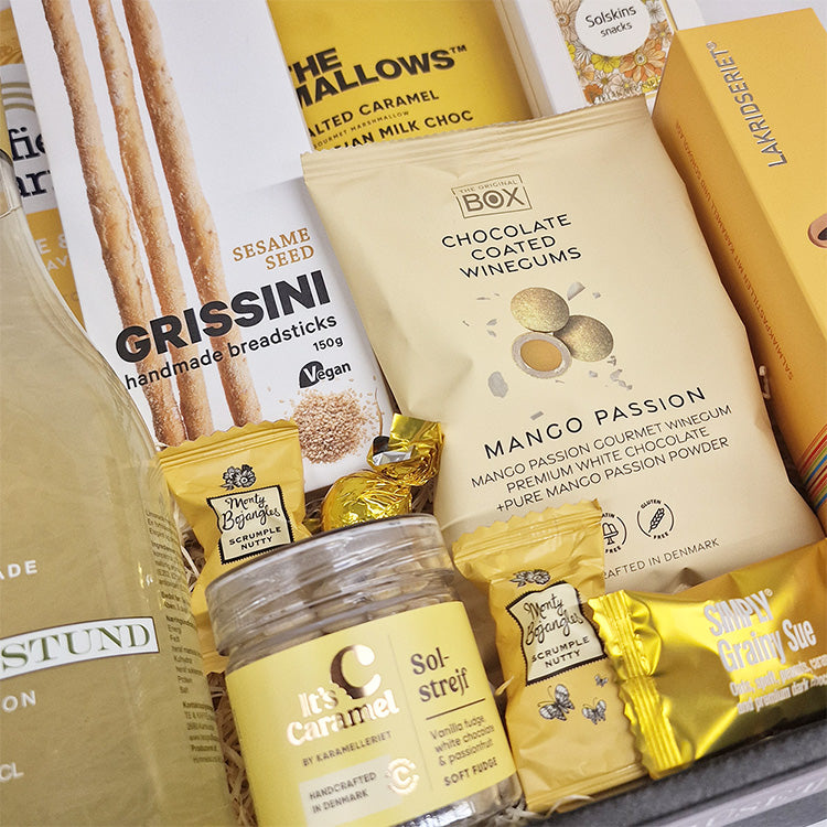 Nærbillede af en gavekurv med gule delikatesser som mango vingummi, grissini og karameller fra Delikatessehuset.