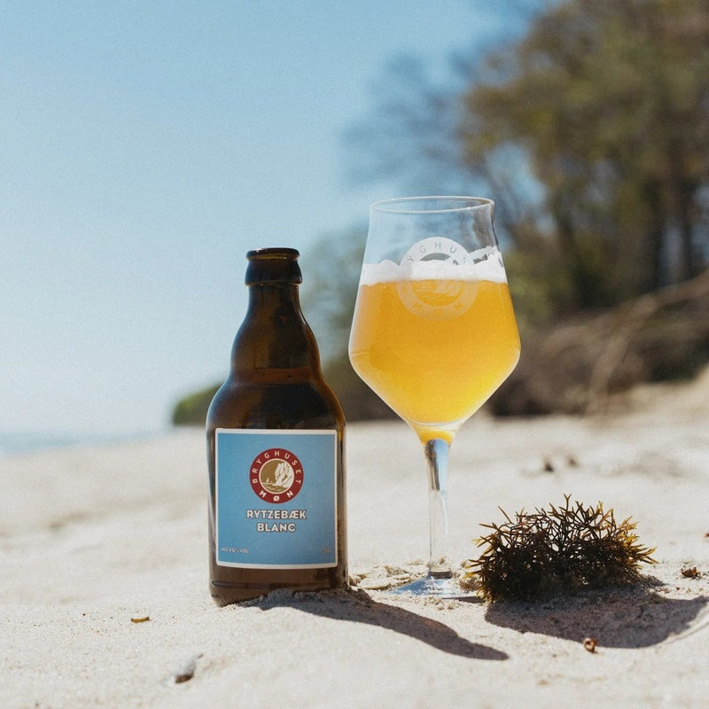 Flaske og glas med Rytzebæk Blanc fra Bryghuset Møn på stranden
